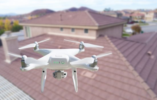 Unmanned Aircraft System (UAV) Quadcopter Drone In The Air Over House Inspecting the Roof. Unmanned Aircraft System (UAV) Quadcopter Drone In The Air Over House Inspecting the Roof.